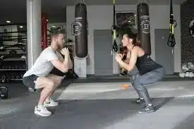 deux personnes font des squats face a face dans une salle de