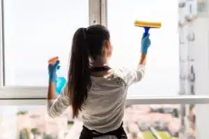 femme en gants bleus nettoyant une fenetre avec un spray et