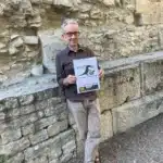 homme tenant une brochure crocamar devant un mur de pierre a