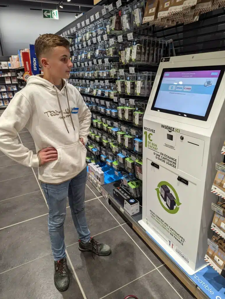 jeune homme devant une borne de recyclage de cartouches d en