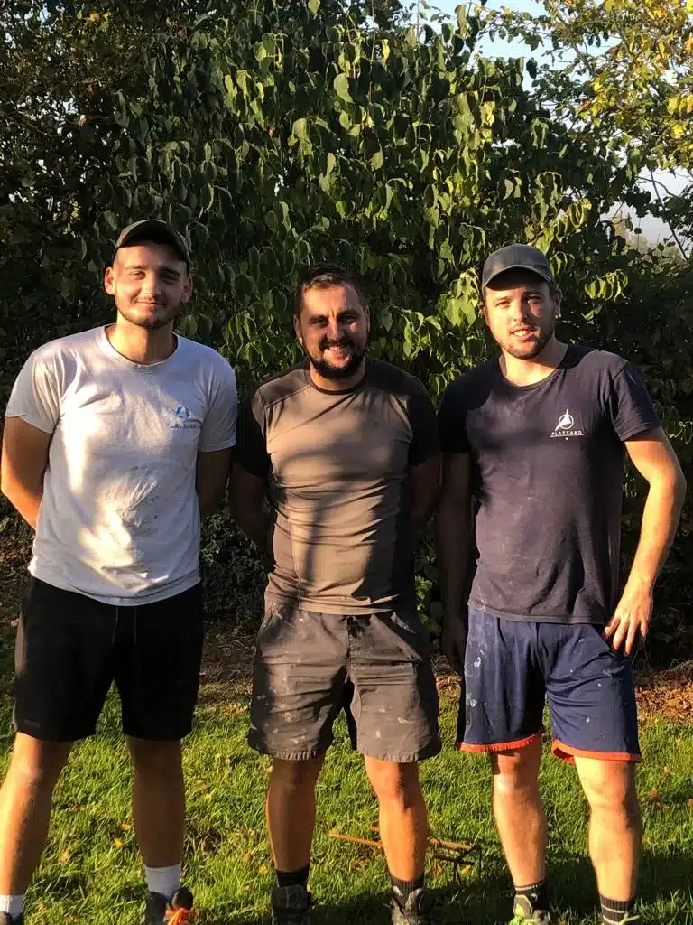 trois hommes en tenue de travail posent devant un feuillage