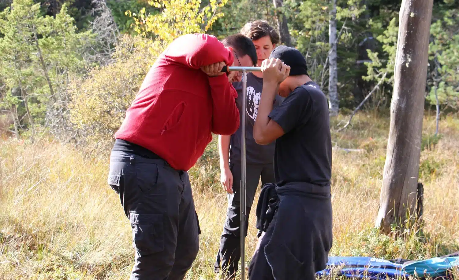 trois jeunes hommes en exterieur penches sur un poteau stage